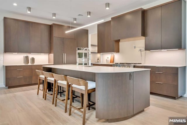 kitchen with a kitchen bar, sink, a center island with sink, light hardwood / wood-style flooring, and range