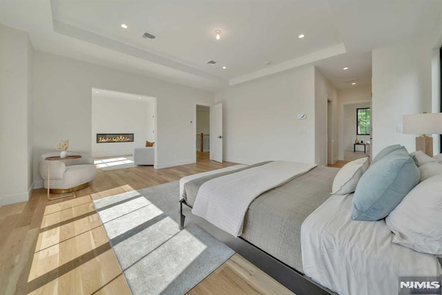 bedroom with a tray ceiling and light hardwood / wood-style flooring