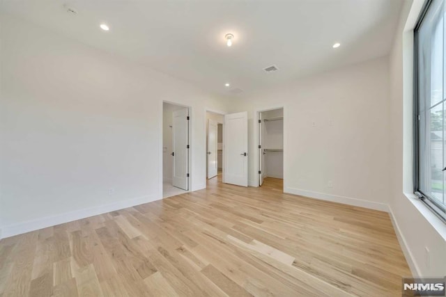 unfurnished bedroom featuring a spacious closet, a closet, and light wood-type flooring