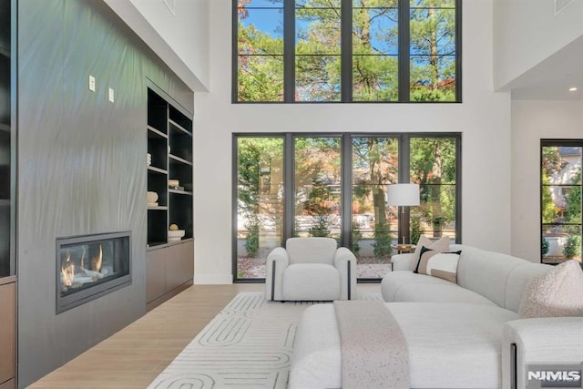 living room with built in features, a large fireplace, wood-type flooring, and a high ceiling