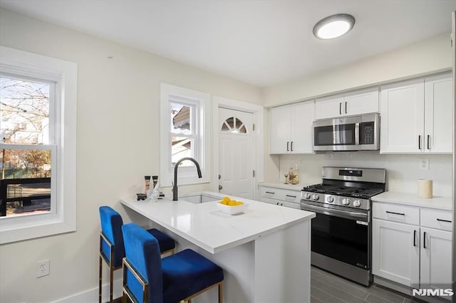 kitchen featuring kitchen peninsula, a kitchen bar, sink, stainless steel appliances, and white cabinets