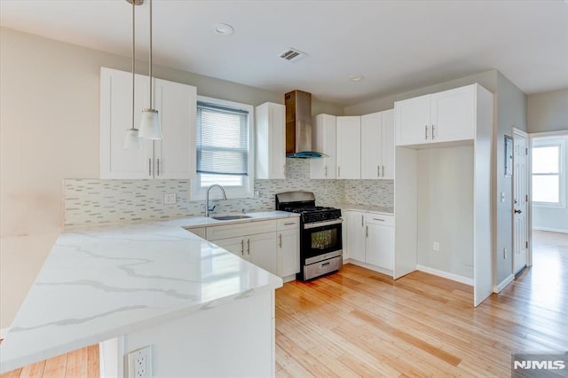 kitchen with stainless steel gas range, decorative light fixtures, white cabinets, and wall chimney range hood