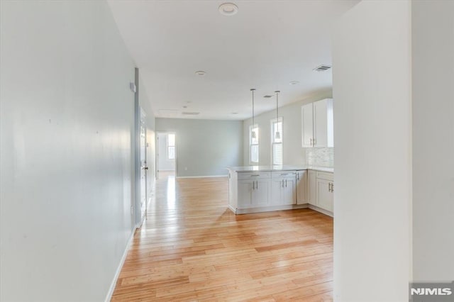 kitchen featuring light hardwood / wood-style flooring, kitchen peninsula, backsplash, and white cabinets