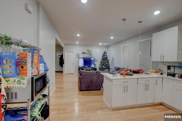 kitchen with white cabinetry, tasteful backsplash, hanging light fixtures, kitchen peninsula, and light wood-type flooring