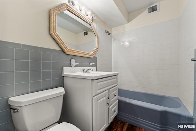 full bathroom with toilet, tiled shower / bath combo, hardwood / wood-style flooring, tile walls, and vanity