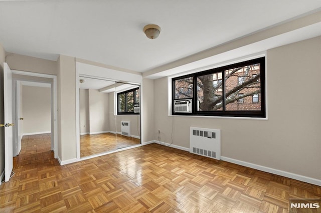 unfurnished bedroom with a closet, radiator heating unit, light parquet floors, and cooling unit