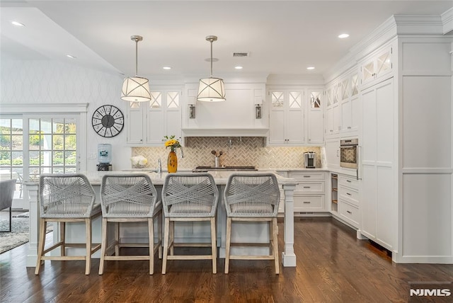 kitchen with pendant lighting, stainless steel oven, white cabinetry, and a kitchen island with sink