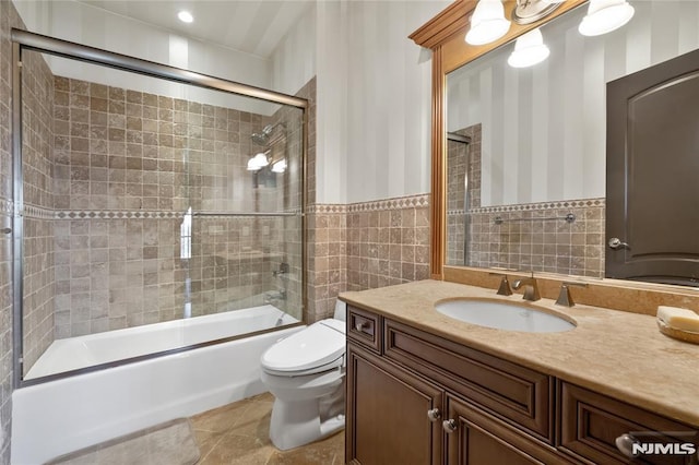 full bathroom featuring toilet, vanity, tile walls, tile patterned floors, and shower / bath combination with glass door