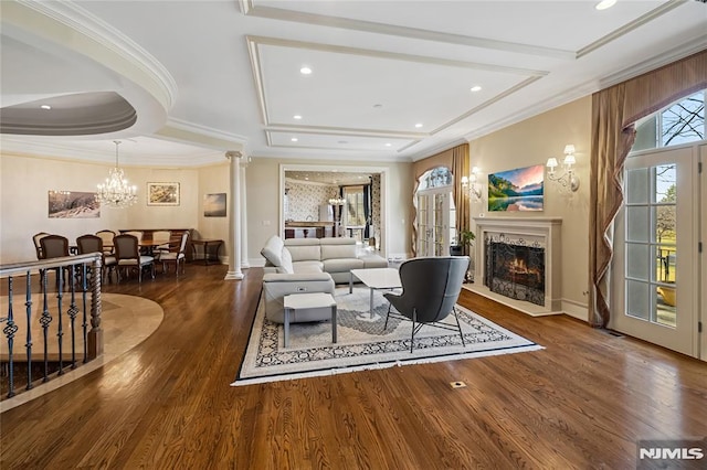 living room with dark hardwood / wood-style flooring, an inviting chandelier, ornamental molding, and decorative columns