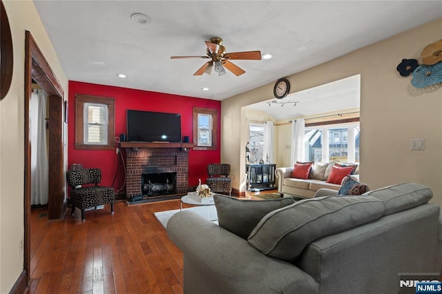 living room featuring a brick fireplace, wood-type flooring, and ceiling fan