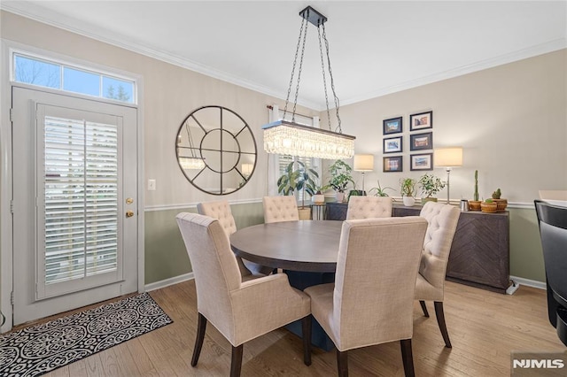 dining space with light wood-type flooring, ornamental molding, and a notable chandelier