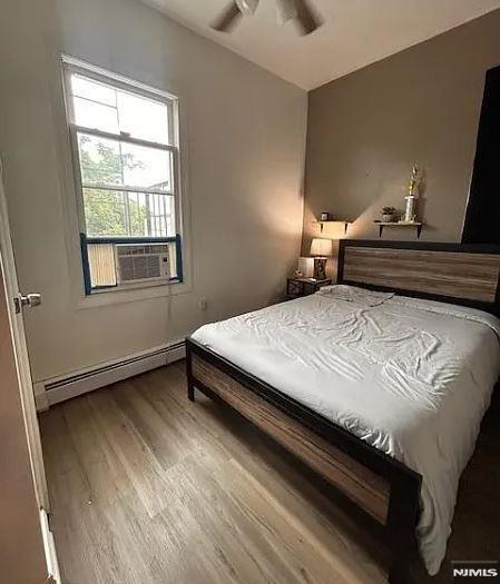 bedroom featuring ceiling fan, cooling unit, wood-type flooring, and a baseboard radiator