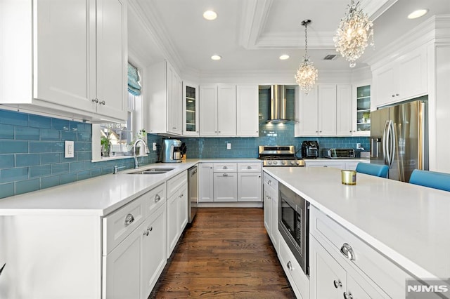 kitchen featuring stainless steel appliances, wall chimney range hood, an inviting chandelier, white cabinetry, and ornamental molding