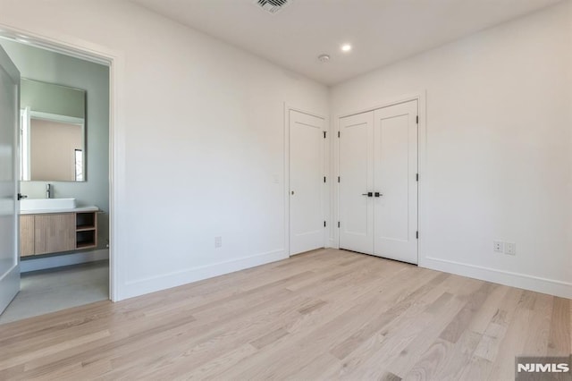 unfurnished bedroom featuring ensuite bathroom, light hardwood / wood-style flooring, and sink