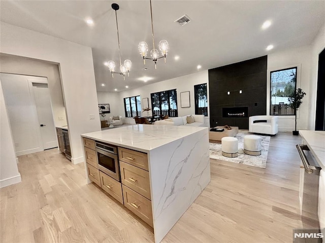 kitchen featuring light stone countertops, pendant lighting, a center island, light wood-type flooring, and stainless steel microwave