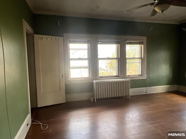 spare room featuring dark wood-type flooring, ceiling fan, and radiator