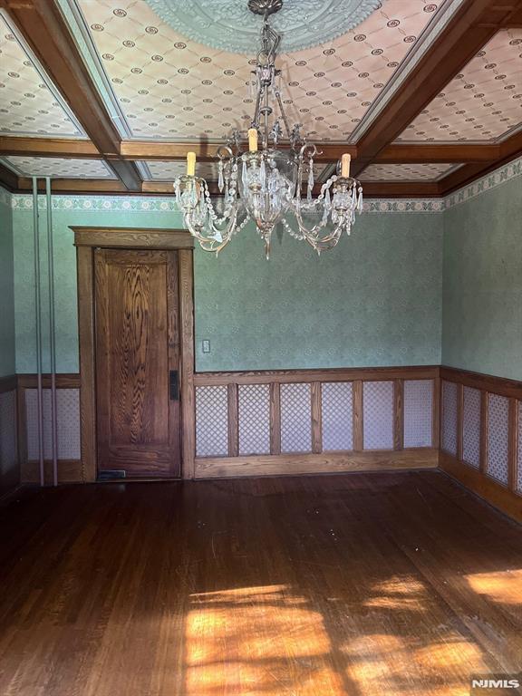 unfurnished room featuring a chandelier, beam ceiling, dark hardwood / wood-style flooring, ornamental molding, and coffered ceiling