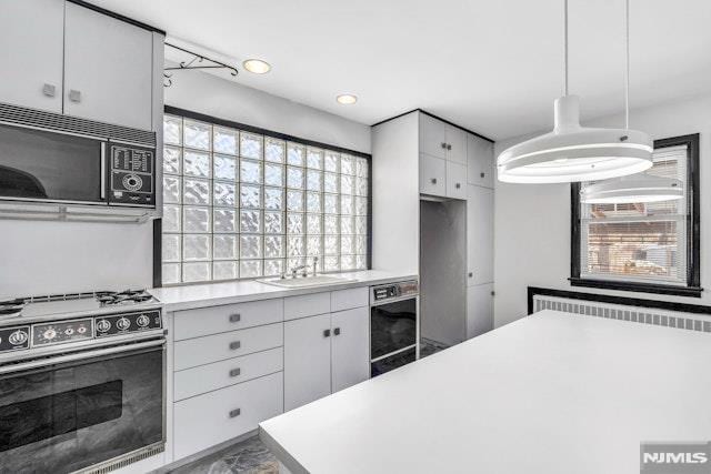 kitchen featuring stove, sink, pendant lighting, and white cabinets