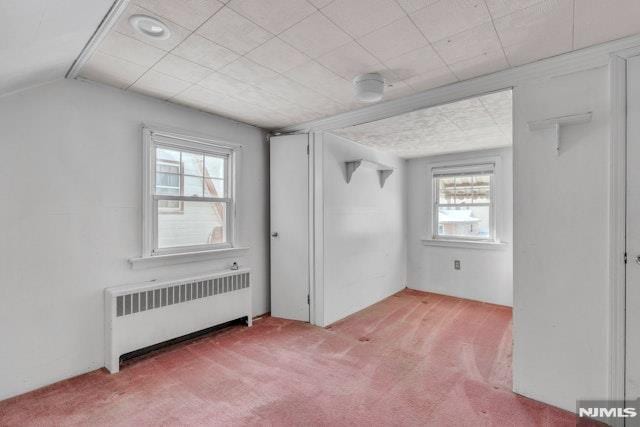 unfurnished bedroom featuring multiple windows, vaulted ceiling, light carpet, and radiator heating unit