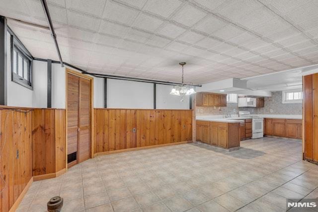 kitchen with hanging light fixtures, wooden walls, white appliances, and kitchen peninsula