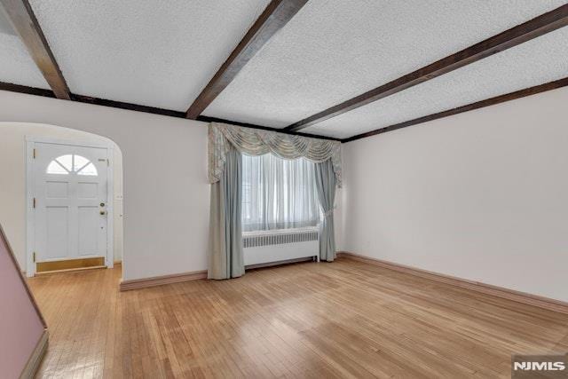 entryway featuring beamed ceiling, radiator, light hardwood / wood-style floors, and a textured ceiling