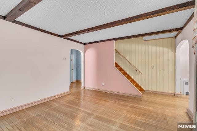 spare room with wood-type flooring, beam ceiling, and a textured ceiling