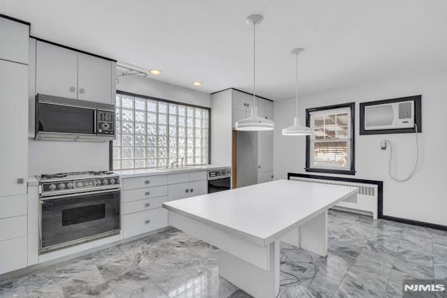 kitchen featuring a breakfast bar, stainless steel gas range oven, hanging light fixtures, radiator, and white cabinets