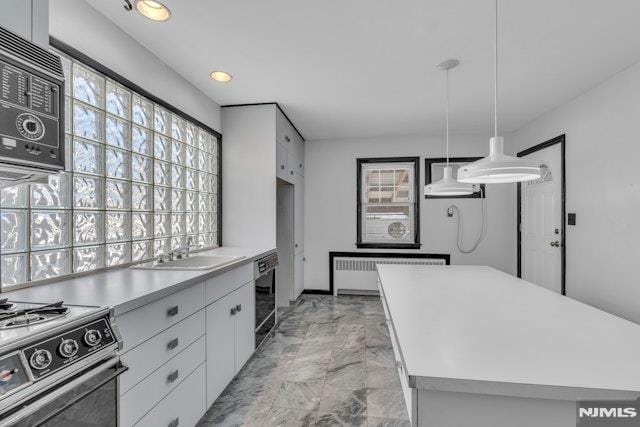 kitchen featuring sink, white cabinetry, radiator heating unit, a kitchen island, and pendant lighting