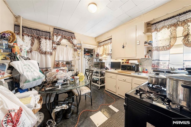 kitchen with black gas range, backsplash, cream cabinets, and sink