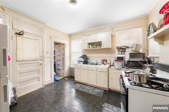 kitchen with radiator, gas range gas stove, fridge, cream cabinetry, and ornamental molding