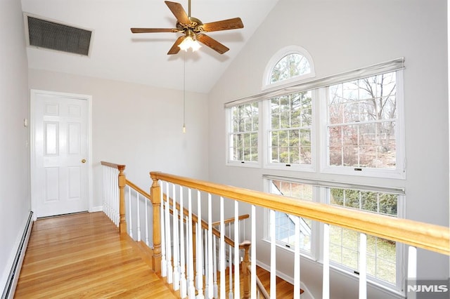 corridor with light wood-type flooring, baseboard heating, and high vaulted ceiling