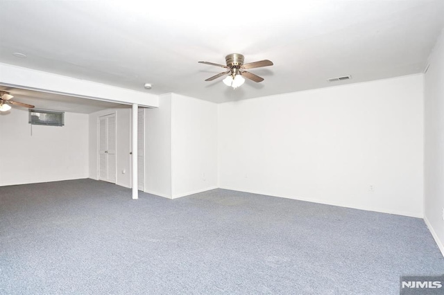 basement with ceiling fan and dark carpet