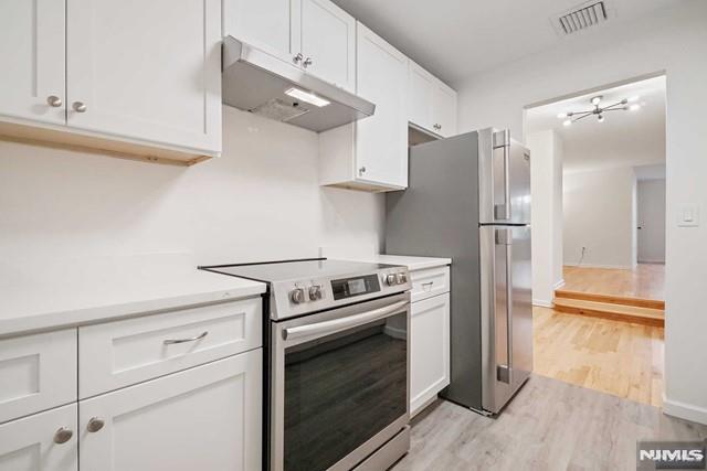 kitchen with white cabinets, light wood-type flooring, and appliances with stainless steel finishes