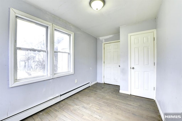 unfurnished bedroom with hardwood / wood-style floors and a baseboard heating unit