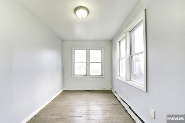 unfurnished room featuring a healthy amount of sunlight, a baseboard radiator, and wood-type flooring