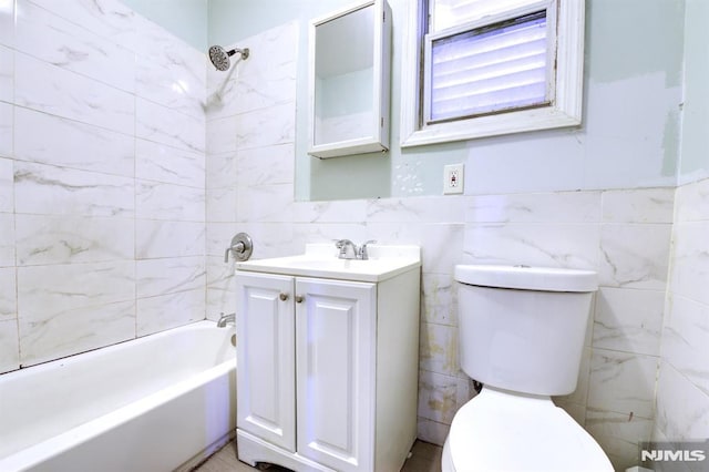 full bathroom with vanity, toilet, tiled shower / bath, and tile walls