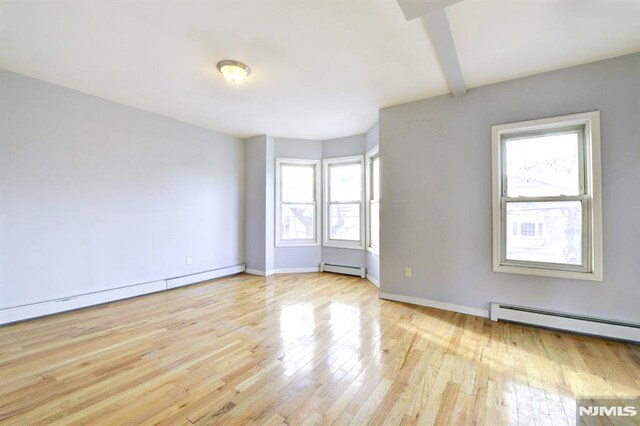 unfurnished room with beamed ceiling, light wood-type flooring, and a baseboard radiator