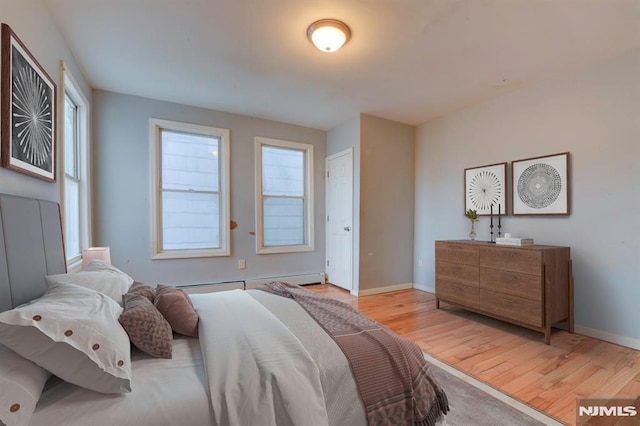 bedroom with light hardwood / wood-style floors and a baseboard heating unit