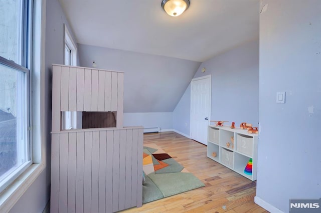 recreation room featuring light wood-type flooring, vaulted ceiling, and a baseboard heating unit