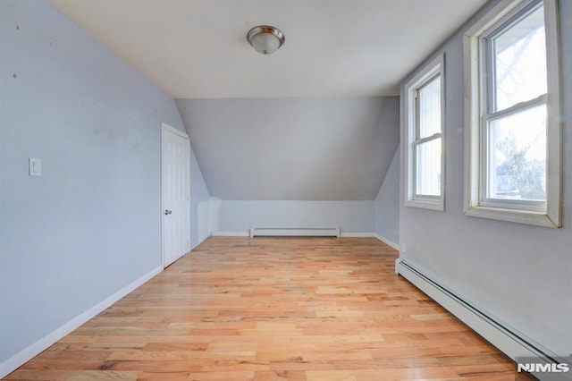 additional living space with lofted ceiling, light wood-type flooring, and a baseboard heating unit