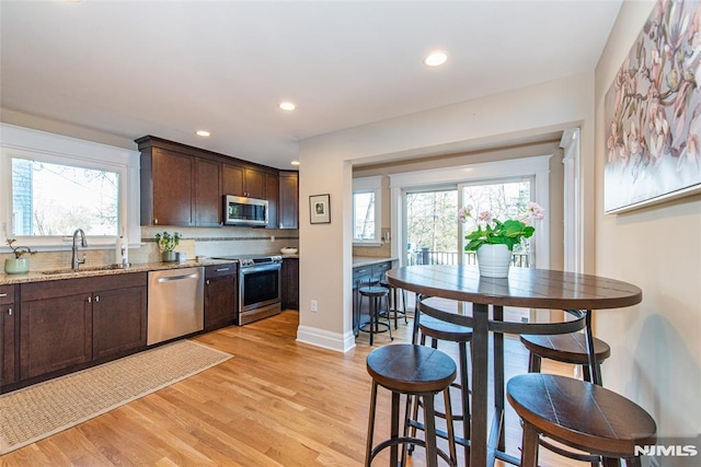 kitchen with appliances with stainless steel finishes, dark brown cabinetry, light hardwood / wood-style floors, and sink