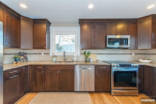 kitchen featuring decorative backsplash, light wood-type flooring, light stone counters, stainless steel appliances, and sink