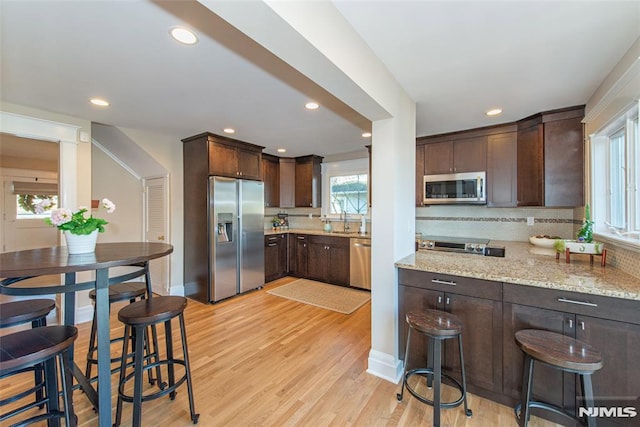 kitchen with backsplash, a breakfast bar area, light stone countertops, dark brown cabinets, and stainless steel appliances