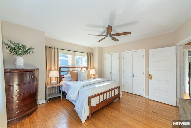 bedroom featuring light hardwood / wood-style flooring, ceiling fan, and multiple closets