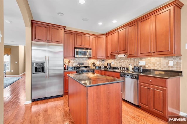 kitchen with a kitchen island, decorative backsplash, sink, light wood-type flooring, and appliances with stainless steel finishes