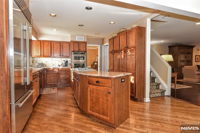 kitchen featuring light stone countertops, stainless steel appliances, a kitchen island, and hardwood / wood-style flooring