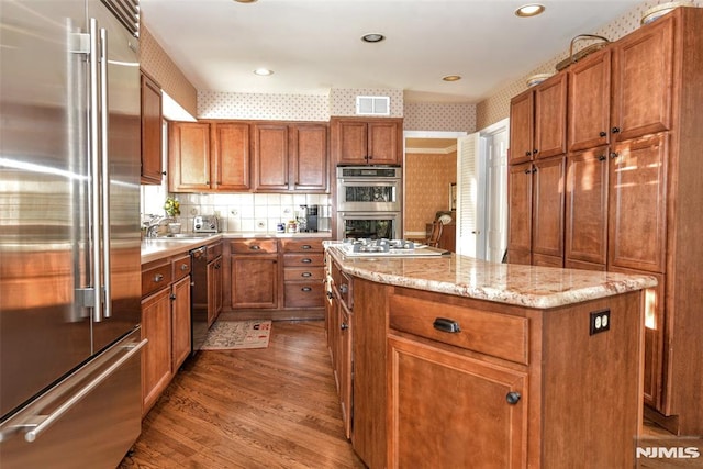 kitchen featuring hardwood / wood-style flooring, light stone countertops, a kitchen island, appliances with stainless steel finishes, and sink