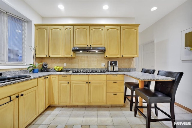 kitchen with light brown cabinetry, light stone countertops, and black gas cooktop