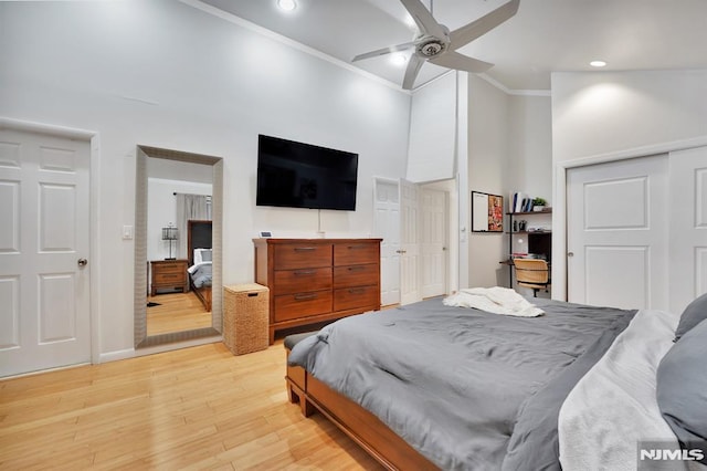 bedroom with a closet, a high ceiling, light hardwood / wood-style flooring, ornamental molding, and ceiling fan