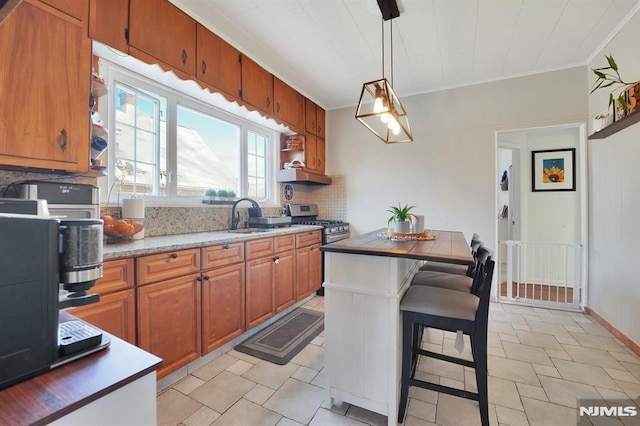 kitchen featuring a kitchen breakfast bar, pendant lighting, stainless steel range with gas stovetop, sink, and decorative backsplash